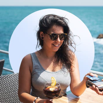 A young woman with sunglasses dining oceanside paying her server with a credit card