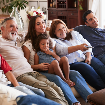 Three generation Hispanic family sitting on the sofa watching TV, grandmother using remote control