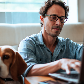 Middle-aged man comfortably working at home on his laptop, sitting on the floor with his Beagle dog by his side.