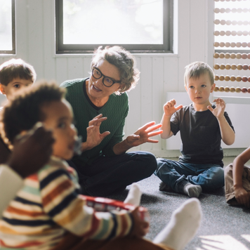 Gray-haired female teacher playing with a group of preschool children.
