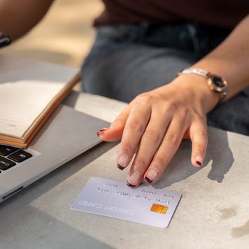 A close-up of a woman's hand holds a credit card above a table while using her laptop.