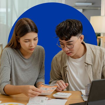 Young couple reviews paperwork at a table, with a laptop open in front of them.