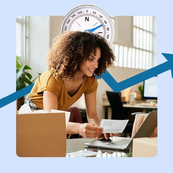 Image of a woman leaning over a desk working on a laptop. There is a large compass behind her head and a blue jagged arrow pointing from the lower left to upper right.
