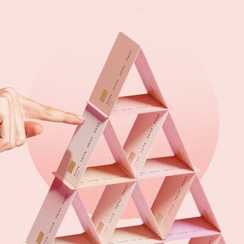 Hand pokes pyramid of stacked credit cards in front of a pink background