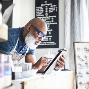 Small-business owner looks at his tablet as he works at the counter of his store.