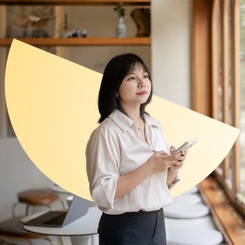 A young woman standing with her phone in her hands, looking off. There is an illustrated semicircle behind her.