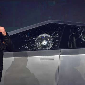 Tesla CEO Elon Musk standing next to a Cybertruck with damaged side windows.