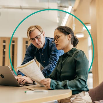 A man and woman in casual business clothes review paperwork in an office conference room.