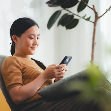 Young woman looks at phone while sitting on a sofa.