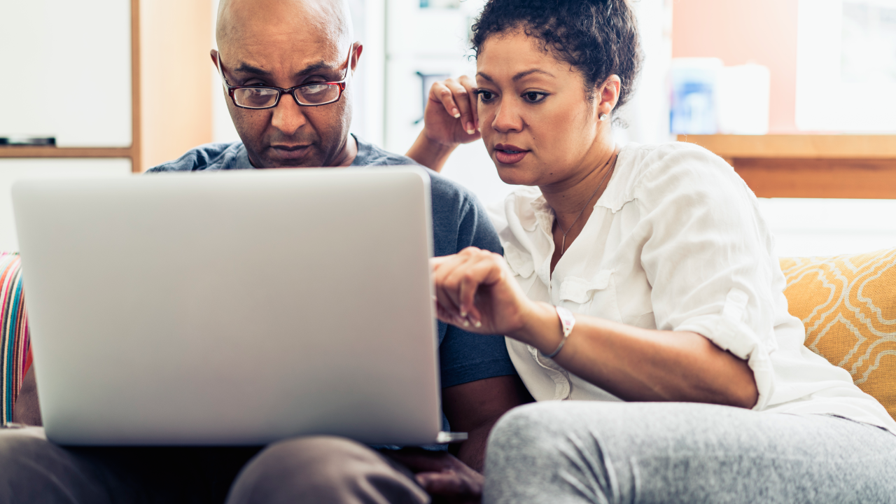 Couple looking at laptop while sitting on sofa at home.