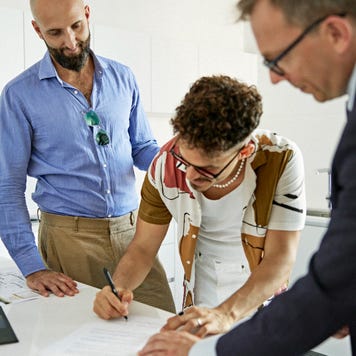 A father and son sign loan documents together while a banker witnesses.
