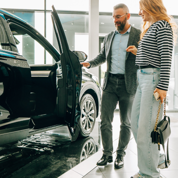 Car salesman showing a new car to a customer in a dealership.