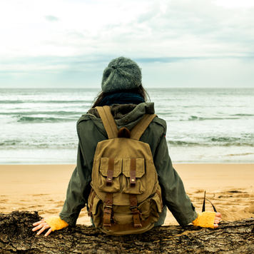 Adult woman sitting on a log contemplating the sea on the beach in the winter