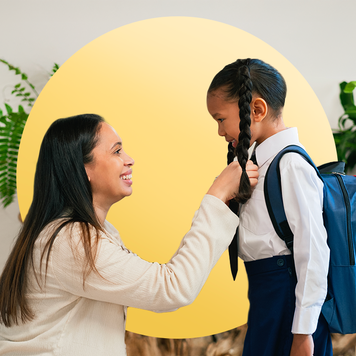Mom in business clothes kneeling down in front of her daughter, who is wearing a backpack, getting ready to send her off to school