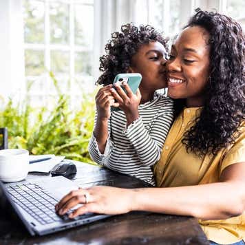 Mother trying to work on laptop while her young daughter is distracting her.