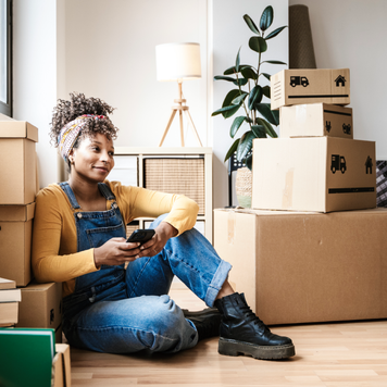 Woman with a cell phone, surrounded by moving boxes.
