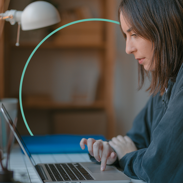 A woman sits at her desk and uses a laptop.