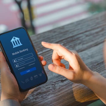 Over the shoulder shot of a woman using her phone. The phone has a mobile banking login screen.