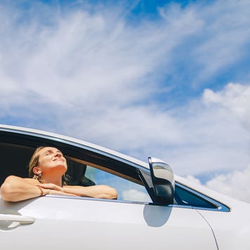 Woman sits relaxed in a car enjoying the sun and the scenic view