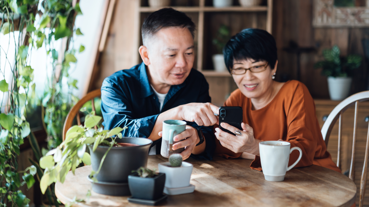 Happy couple sitting at a table at home, managing their finances on a smartphone together.