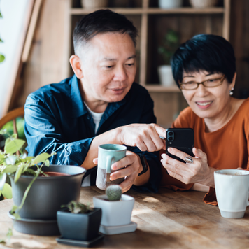 Happy couple sitting at a table at home, managing their finances on a smartphone together.