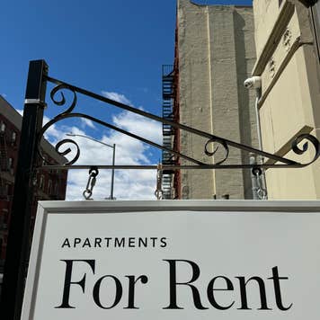 A For Rent sign hangs in front of a city apartment building