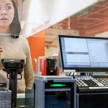 Young female customer talking to cashier at checkout in supermarket