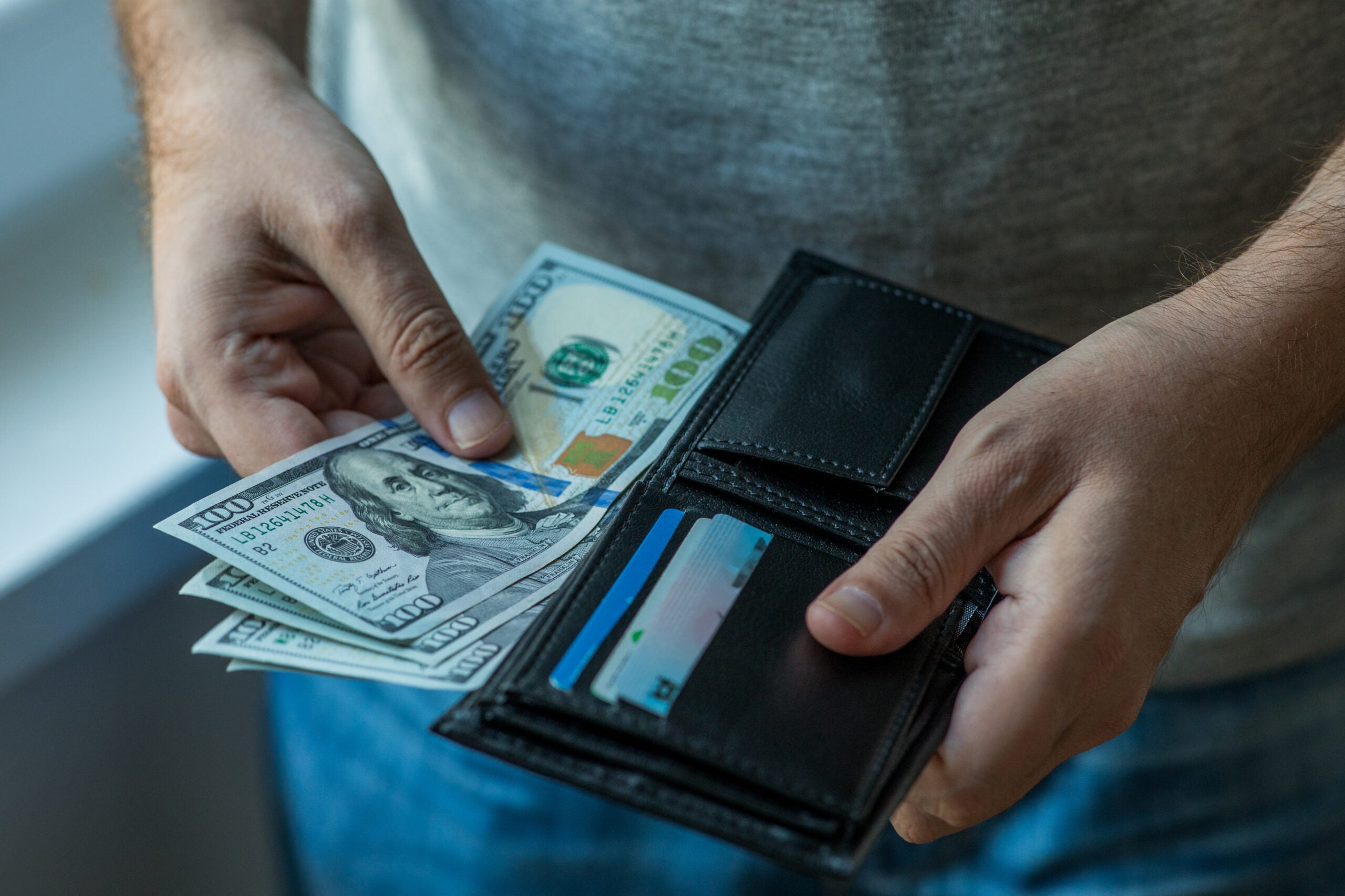 Close up on hands pull $100 bills out of a wallet