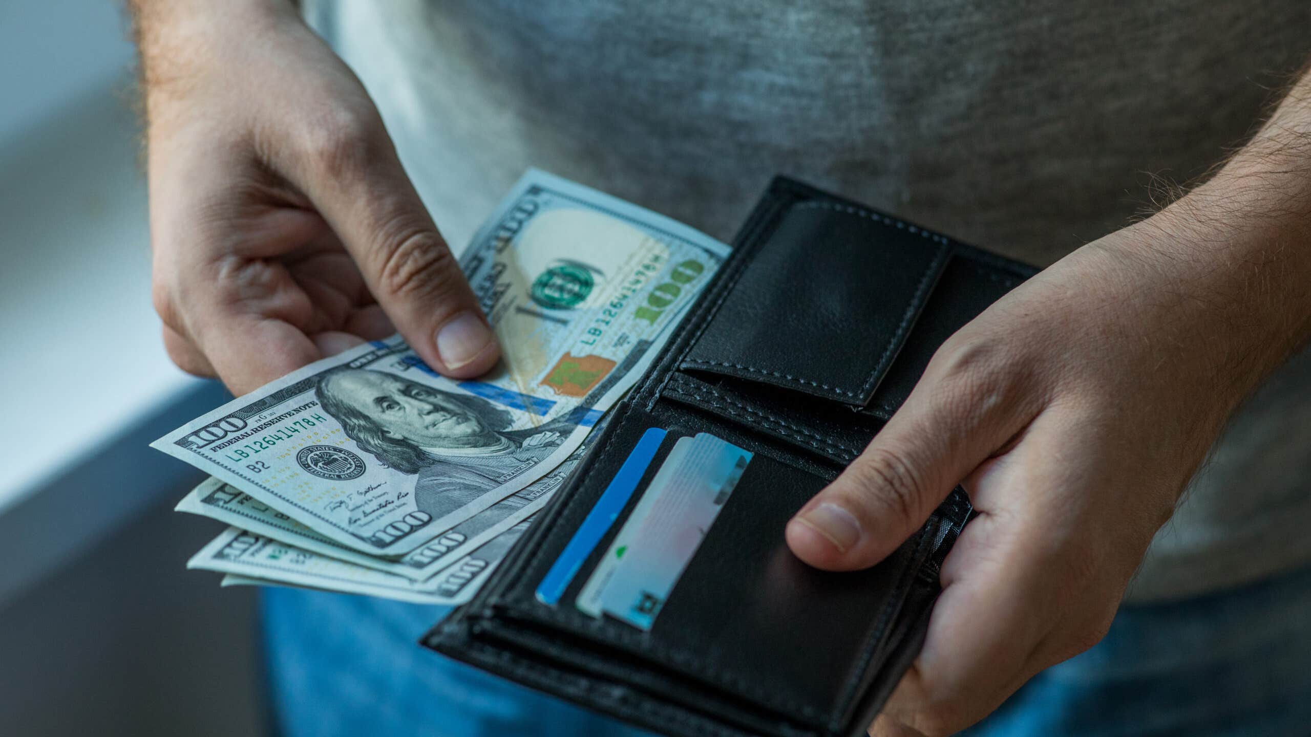 Close up on hands pull $100 bills out of a wallet