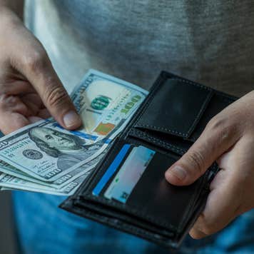 Close up on hands pull $100 bills out of a wallet