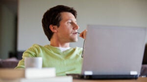 Man sitting in front of his laptop looking pensive while holding his glasses.