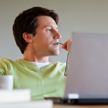 Man sitting in front of his laptop looking pensive while holding his glasses.