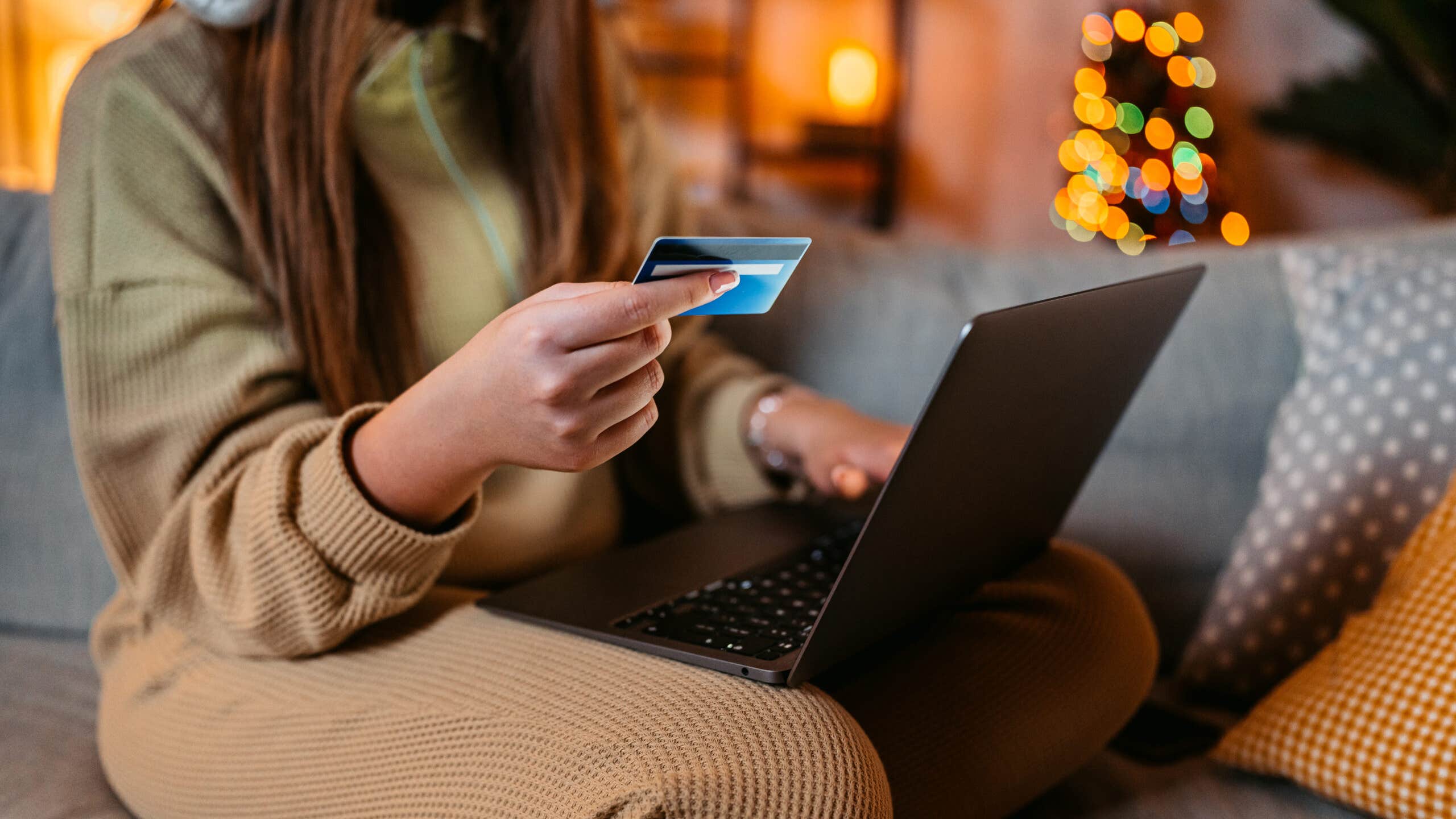 A woman holds a credit card and online shops with holiday lights in the background