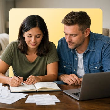 A man and woman sit close together and look at books and a computer.