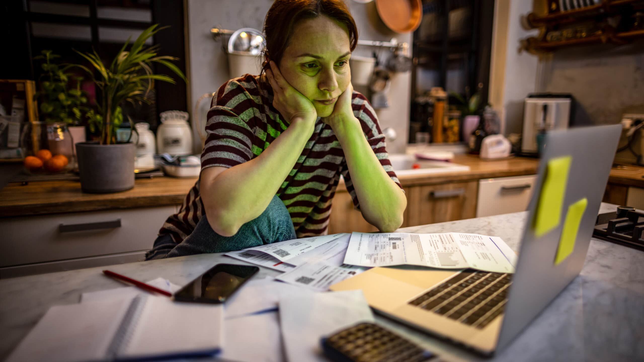 Woman doing her bills in dim light at a kitchen table.