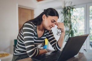 Woman looks stressed with her head in her hand at a laptop.