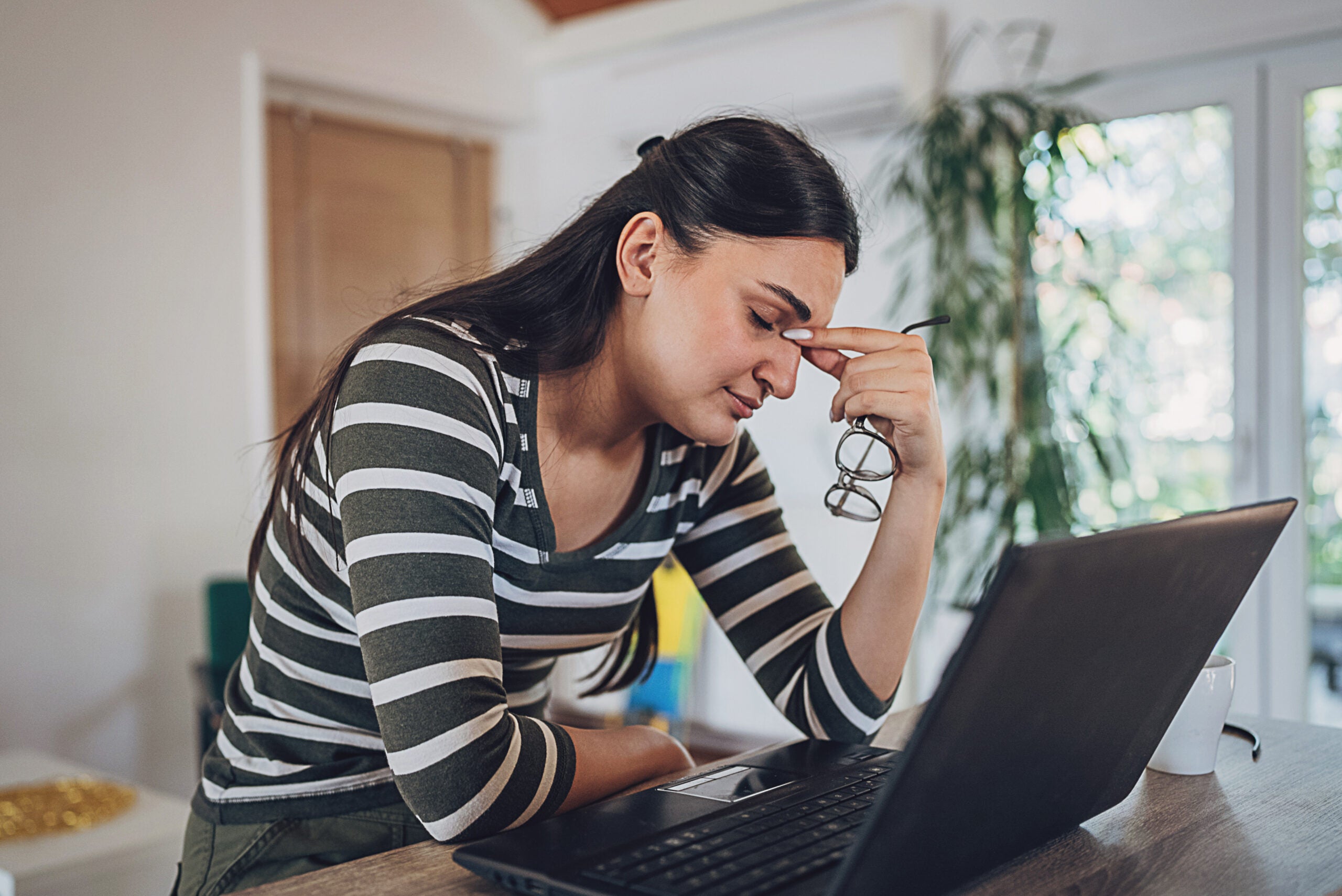 Woman looks stressed with her head in her hand at a laptop.