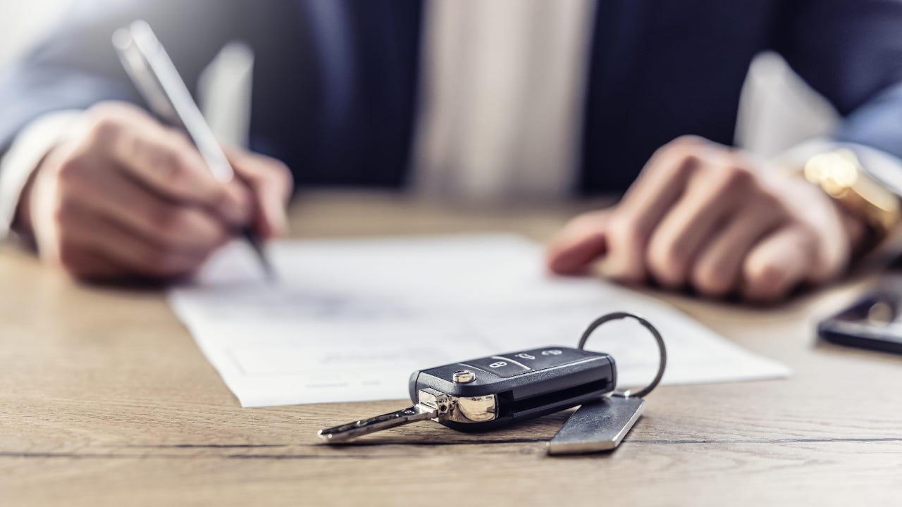 A set of hands signing a document. In the foreground, there is a set of car keys.