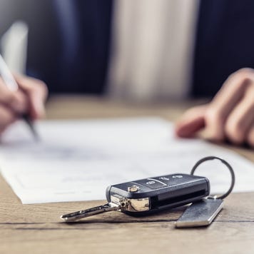 A set of hands signing a document. In the foreground, there is a set of car keys.
