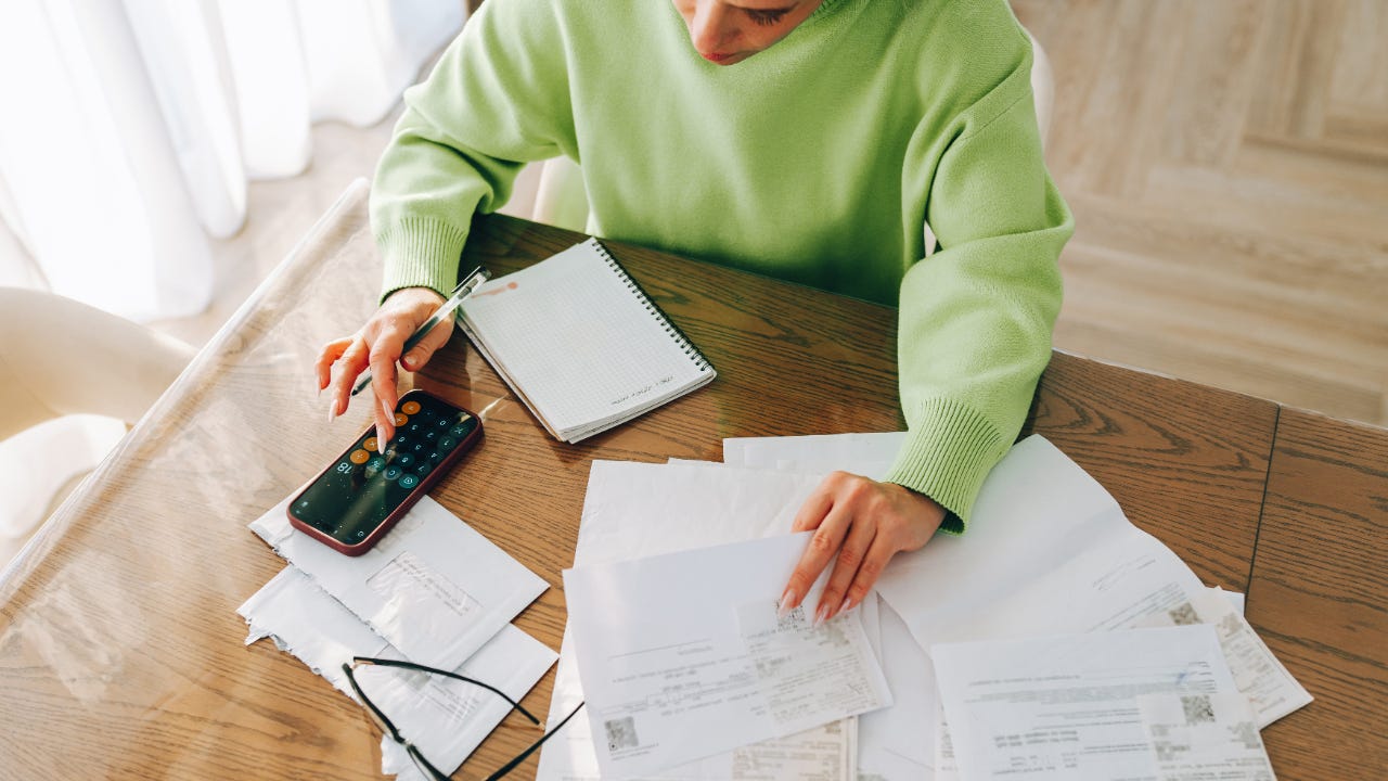 A woman sits at a table and reviews a large stack of bills.
