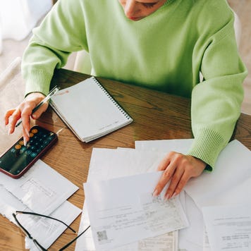 A woman sits at a table and reviews a large stack of bills.