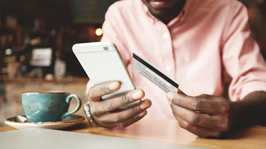 Man sitting at table holding credit card and cell phone