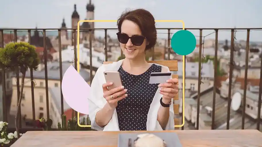 A woman holding a phone in one hand and a credit card in the other hand. She appears to be ready to make an online payment or complete a mobile transaction.
